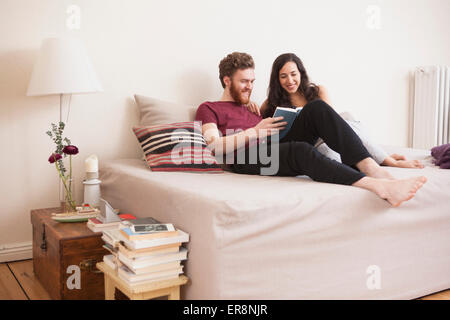 Happy young man reading book for woman in bed