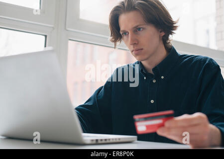 Young man holding credit card while using laptop at table Stock Photo