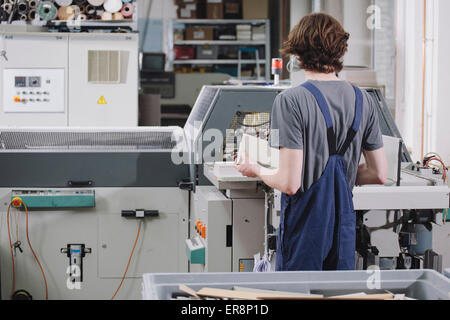 Rear view of young male worker operating machine in factory Stock Photo