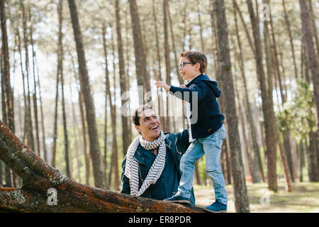 Happy father assisting son in climbing tree at forest Stock Photo