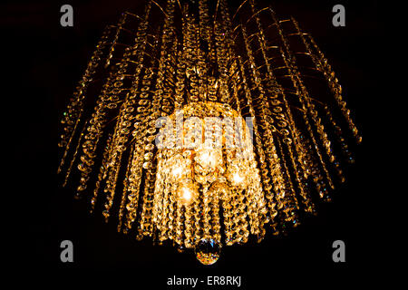 a crystal chandelier glows with golden light on dark background Stock Photo
