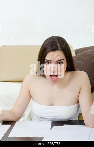 Leasure concept - upset teenage girl woman writes with pen on white paper and sitting on floor at home. Shocked and unhappy fema Stock Photo