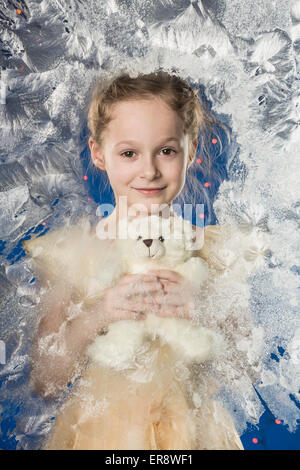 Portrait of cute girl holding teddy bear against frozen glass Stock Photo