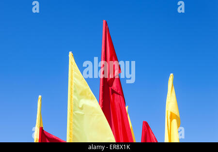 Red and yellow flags fluttering in the wind against blue sky Stock Photo