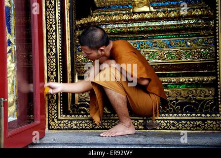 Bangkok, Thailand :  A Buddhist monk in an orange robe cleaning a glass paneled Ubosot Sanctuary Hall doorway Stock Photo