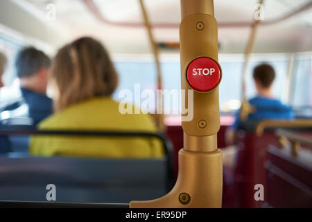 Detail of red stop button inside double decker bus in London, UK, with passengers seated in the blurred background. Stock Photo