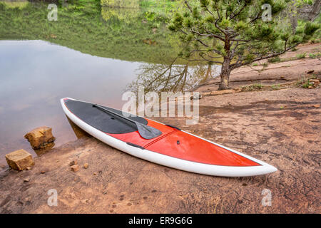 red stand up paddleboard  with a paddle on rocky lake shore - old sandstone quarry at Horsetooth Reservoir Stock Photo