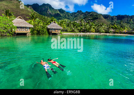 Young couple snorkeling over reef next to resort on a tropical island with over-water villas Stock Photo