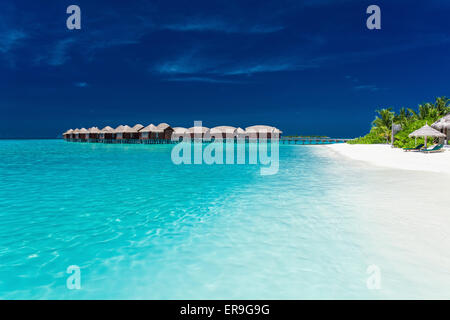 Overwater bungallows in blue lagoon on tropical island with palm trees Stock Photo