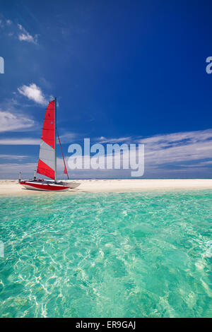 Sailing boat with red sail on beach of deserted tropical island Stock Photo