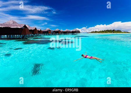 Young woman swimming from hut in blue tropical lagoonYoung couple snorkling from hut over blue tropical lagoon Stock Photo