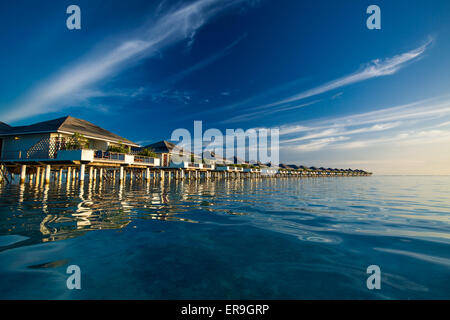 Over water villas in Maldives reflected in blue lagoon before sunset Stock Photo