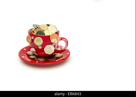 'My cup runneth over'a white cup and saucer full of GBP British coins spilling out.a UK money finance economy coins wealth Stock Photo