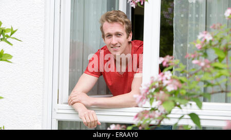 portrait of a young blond man looking out of a window Stock Photo