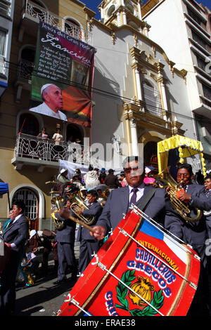 La Paz, Bolivia, 30th May 2015. A brass band passes a banner of Pope Francis hanging outside the Sanctuary of El Señor del Gran Poder during parades for the Gran Poder festival. Pope Francis will visit La Paz during his 3 day trip to Bolivia planned for July 2015. The festival in honour of El Señor del Gran Poder takes place today and is the biggest festival in La Paz. Stock Photo