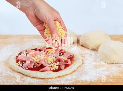 Cook sprinkling shredded cheese over pizza Stock Photo