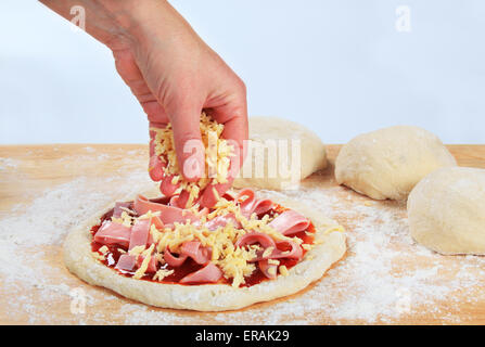 Cook sprinkling shredded cheese over pizza Stock Photo