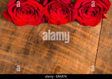 Three bright red roses on a wooden table Stock Photo