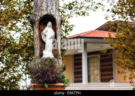 Statue of the Our Lady in hollow trunk the garden in front of the church dedicated to the Blessed Virgin Mary in the village of Stock Photo