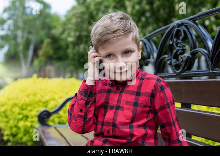 little boy in red shirt talking on cell phone outdoors. Boy smiles Stock Photo