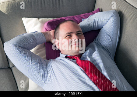 fat man in shirt and tie lying on couch and smiles Stock Photo