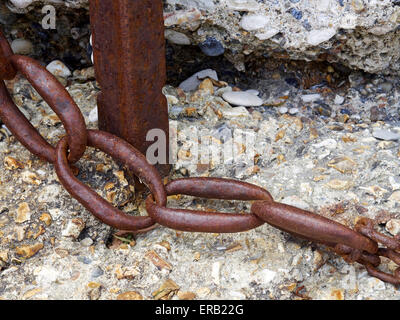 Rusting post and rusty and worn chain against a bettered concrete sea wall at Lulworth Cove Stock Photo