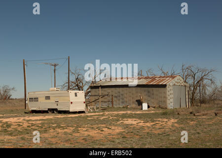 A photograph of an abandoned trailer and barn in West Texas. Taken on a sunny day with no clouds in the sky. Stock Photo