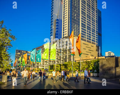 Crowds of people strolling along the flag bedecked Promenade of Southbank waterfront, in the late afternoon Melbourne Australia
