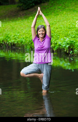 older woman doing yoga in a river Stock Photo