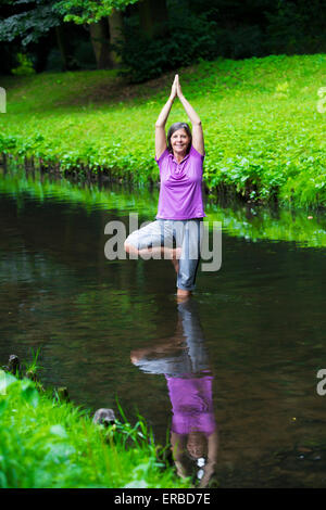 older woman doing yoga in a river Stock Photo