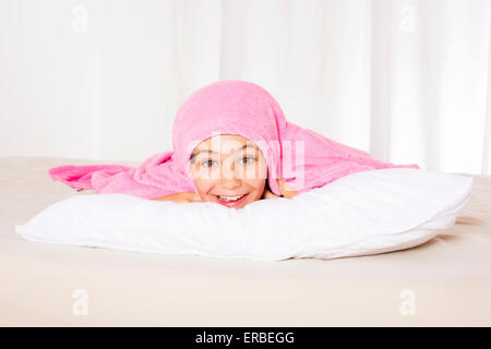 young kid lying in bed and hiding under a pink blanket Stock Photo