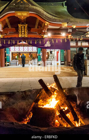 New year's eve at the Shinto Nishinomiya shrine in Japan. Early evening before the crowds. Bonfire in foreground with lone man opraying at shrine hall. Stock Photo
