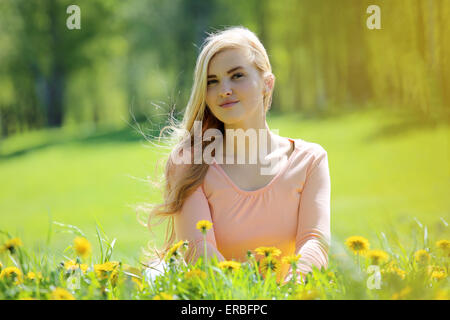 Beautiful young woman laying in spring park with dandelion flowers Stock Photo