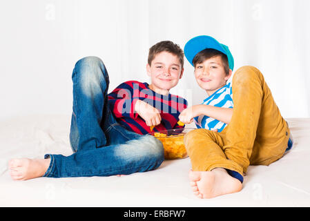 two kids in bed eating potato chips and smiling Stock Photo