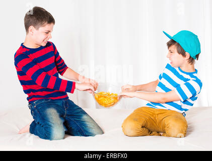 two young boys in bed and fighting over a bowl of potato chips Stock Photo