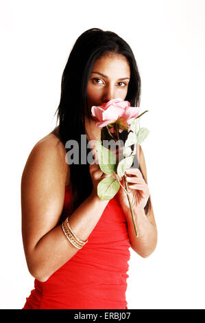 A pretty teenager girl in a red strapless dress standing in the studio for white background, holding a pink rose. Stock Photo