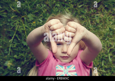 Displeased girl gesturing thumbs down lying on green grass background Stock Photo