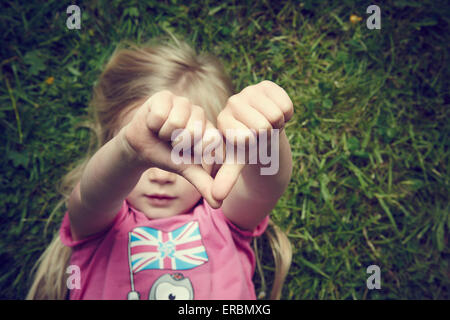 Displeased girl gesturing thumbs down lying on green grass background Stock Photo