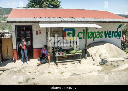 older Mexican woman & teen girl next to fruit stand outside roadside grocery emblazoned with large Green Chiapas foundaton logo