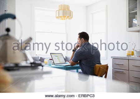 Serious brunette man using laptop at kitchen table