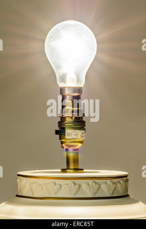 Old type of incandescent electric light bulb in a lamp, turned on, with light rays emanating.