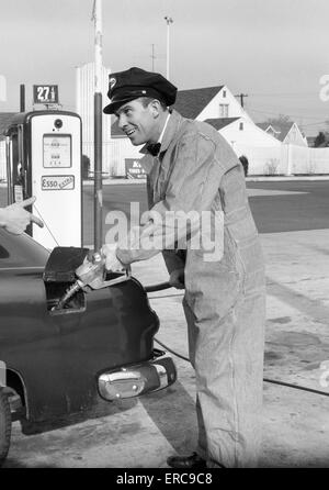 1950s SERVICE STATION ATTENDANT MAN IN STRIPED OVERALLS & CAP FILLING GAS TANK OF AUTOMOBILE Stock Photo