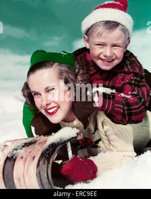 1940s 1950s SMILING TEENAGE GIRL SISTER AND YOUNGER BOY BROTHER LOOKING AT CAMERA RIDING TOBOGGAN DOWNHILL Stock Photo