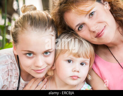 Outdoor summer closeup portrait of a real Caucasian family, young mother with her two daughters Stock Photo