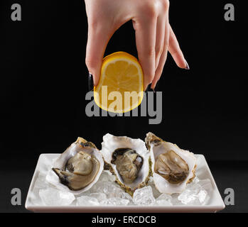 Woman's hand squirt three oyster shell with lemon juice, dark background Stock Photo