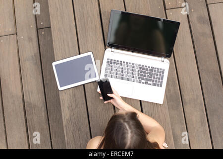 Woman using multiple devices phone laptop and tablet lying in a wood bench in a park Stock Photo