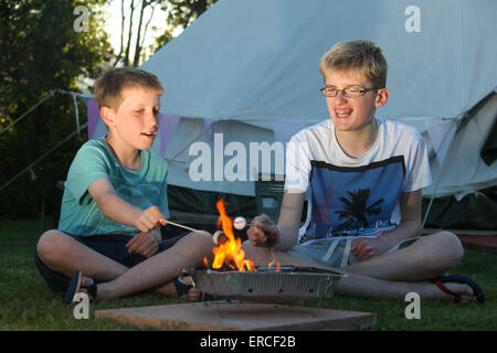 Children toasting marshmallows over a camp fire whilst glamping camping in the UK Stock Photo