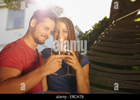 Outdoor shot of young caucasian couple in backyard toasting wine smiling. Romantic couple relaxing on hammock celebrating with w Stock Photo