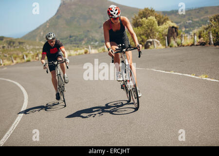 Cyclist riding bikes on open road. Triathletes cycling down the hill on bicycles. Practicing for triathlon race on country road. Stock Photo