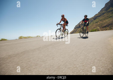 Athletes competing in the cycling leg of triathlon. Triathletes cycling on open country roads. Cyclist riding downhill. Stock Photo